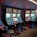 A row of brightly lit slot machines in a casino setting, each with colorful displays and various game themes. The machines are lined up against a dark wall and are unoccupied, with cushioned chairs placed in front of them. The area is dimly lit except for the glow from the screens, creating a vibrant and engaging atmosphere.